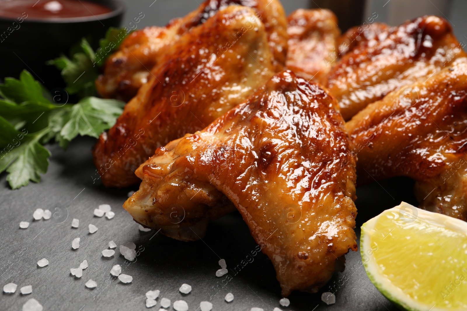 Photo of Delicious fried chicken wings and lime on black table, closeup