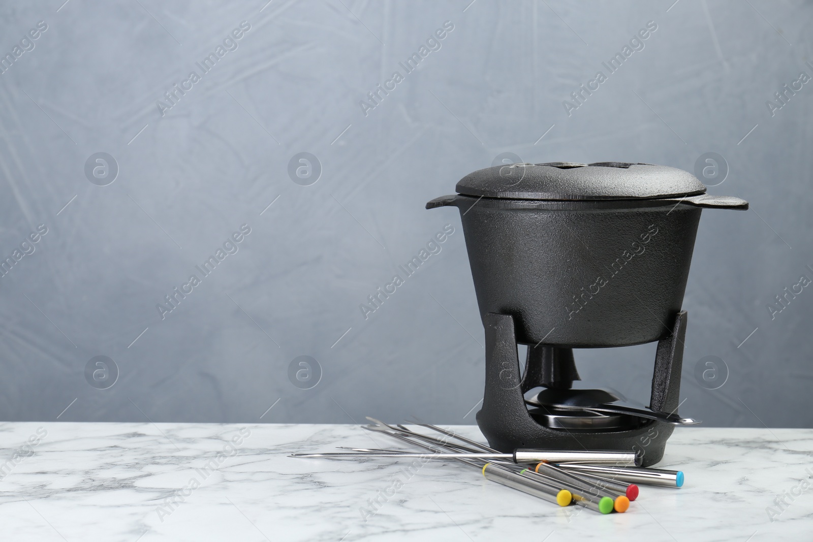 Photo of Fondue set on white marble table against light grey background, space for text