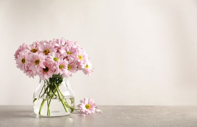 Photo of Vase with beautiful chamomile flowers on table against light background. Space for text