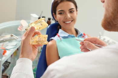 Professional dentist showing patient jaws model in clinic, closeup