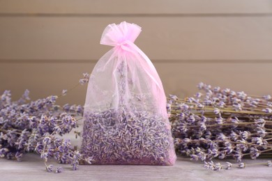 Scented sachet and dried lavender flowers on wooden table, closeup