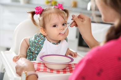 Photo of Mother feeding her little baby with healthy food in kitchen