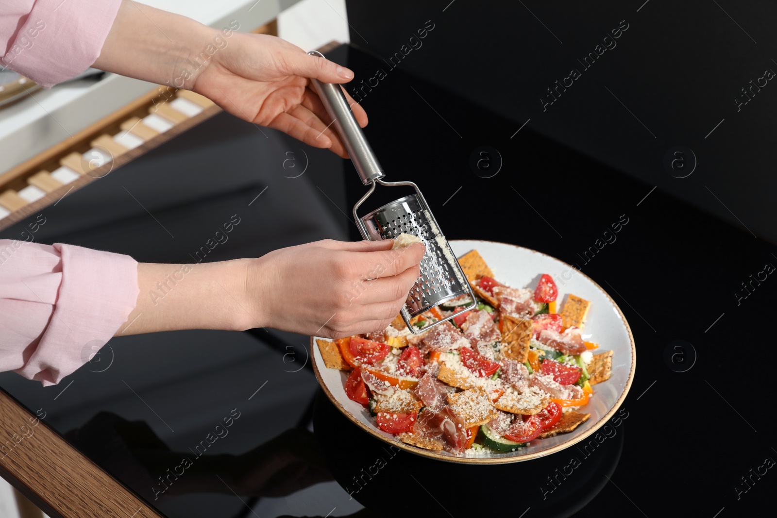 Photo of Food stylist grating cheese onto salad with prosciutto at black table in photo studio, closeup