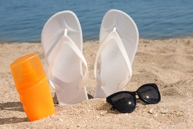 Stylish flip flops, sunglasses and sun protection spray on sandy beach