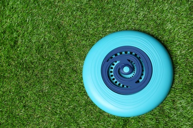 Light blue plastic frisbee disk on green grass, top view. Space for text