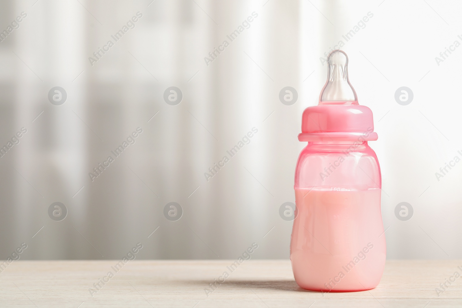 Photo of Feeding bottle with milk on white wooden table indoors