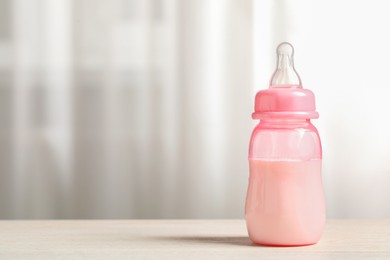 Photo of Feeding bottle with milk on white wooden table indoors