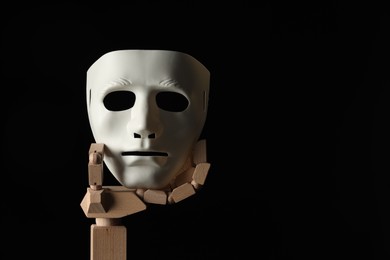 Photo of Wooden mannequin hand holding plastic mask on black background, space for text. Theatrical performance