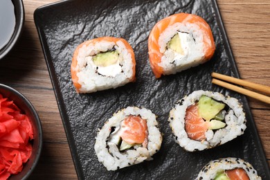 Photo of Delicious sushi rolls, soy sauce, ginger and chopsticks on wooden table, flat lay
