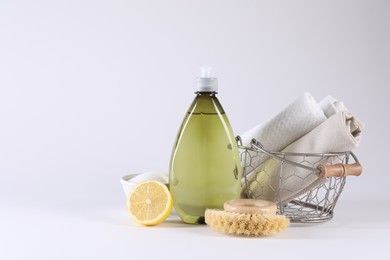 Bottle of cleaning product, brush, rags and lemon on light background