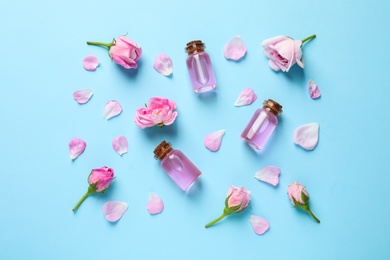 Fresh flowers, petals and bottles of rose essential oil on color background, flat lay