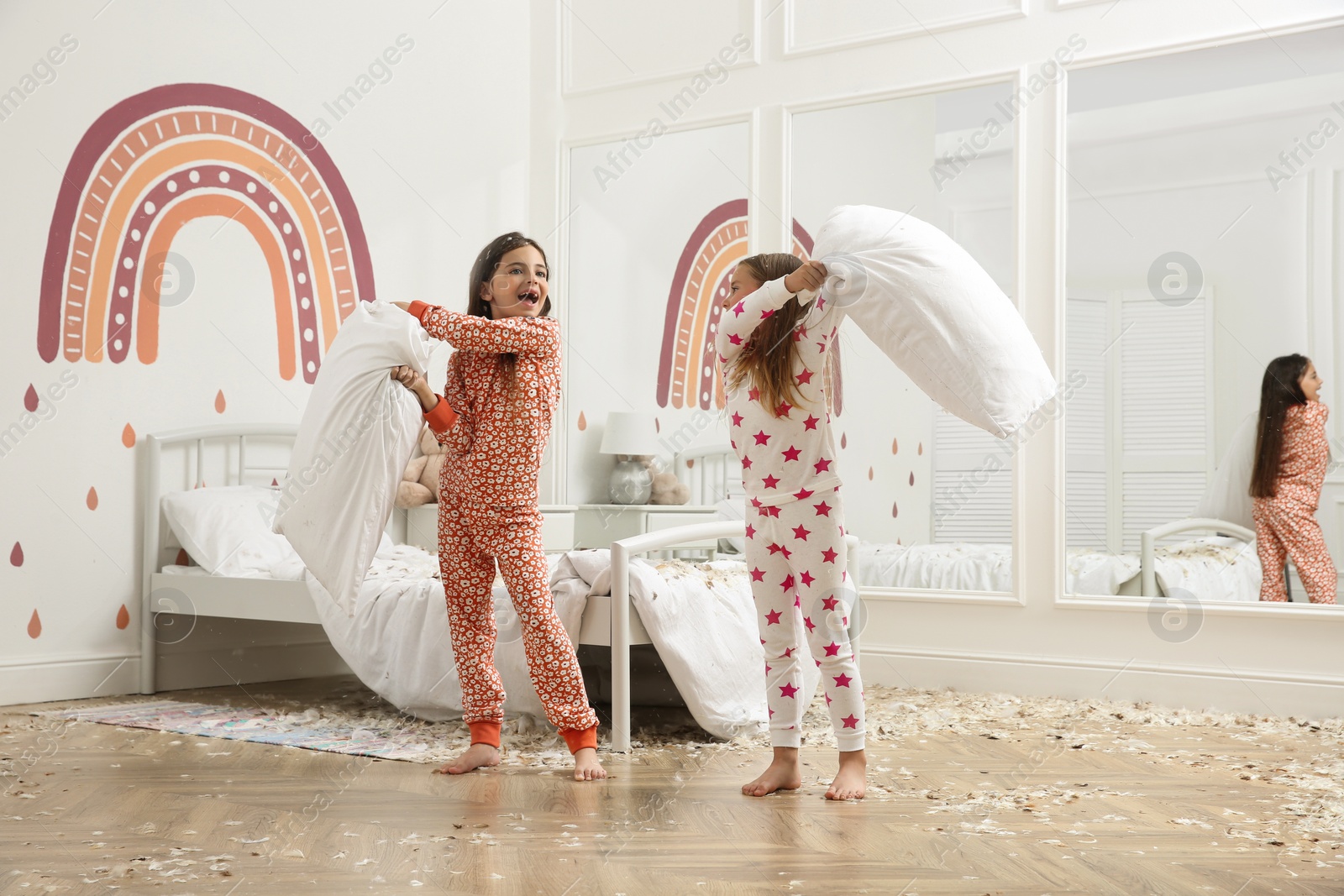 Photo of Cute little girls in pajamas having pillow fight on bed at home. Happy childhood