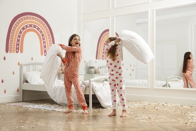 Photo of Cute little girls in pajamas having pillow fight on bed at home. Happy childhood