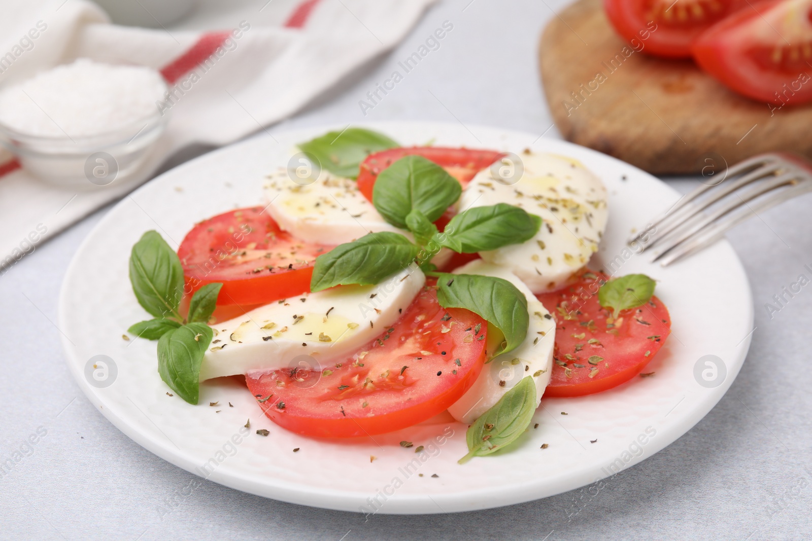 Photo of Plate of delicious Caprese salad with herbs on light grey table, closeup