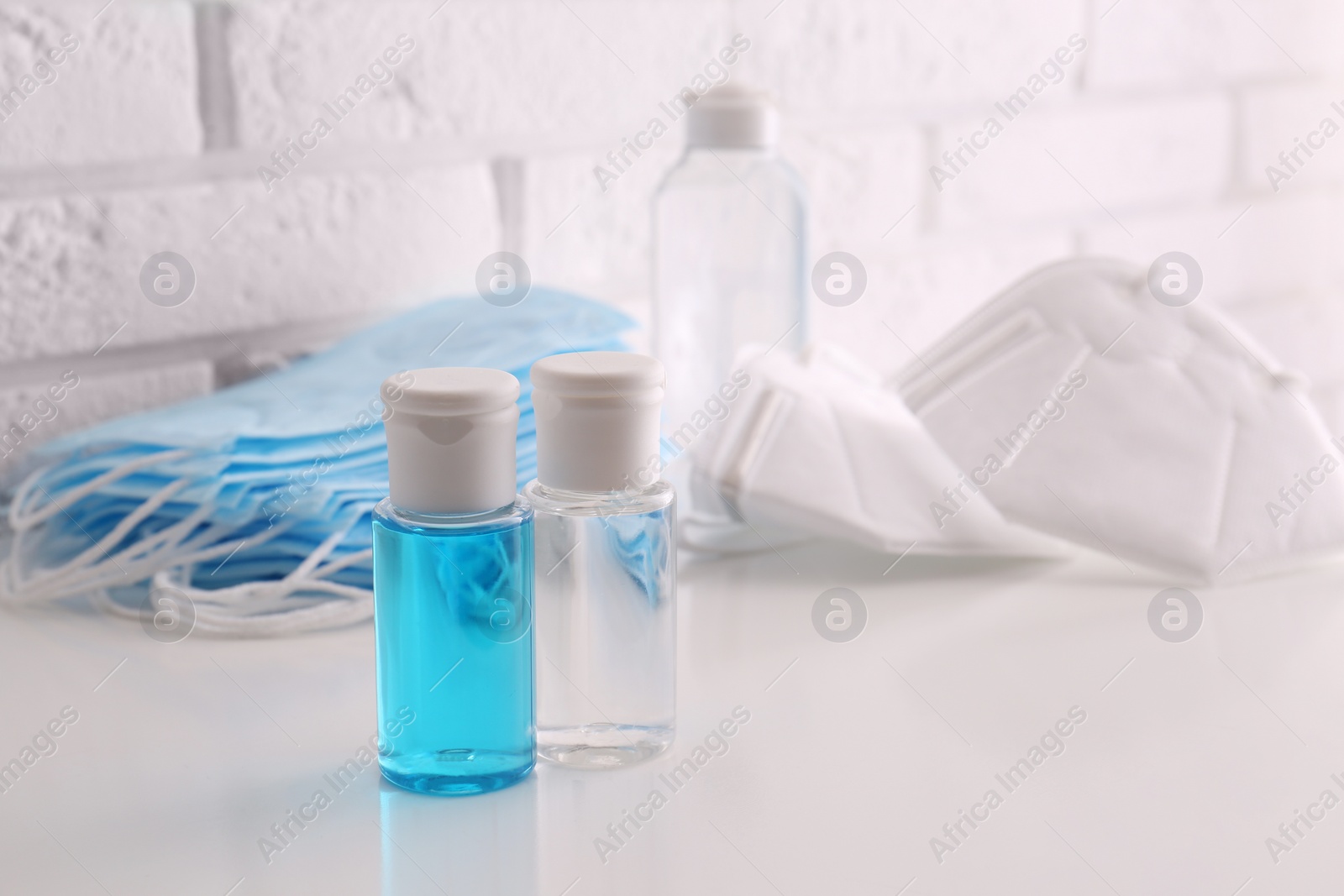 Photo of Hand sanitizers and respiratory masks on table near white brick wall. Protective essentials during COVID-19 pandemic