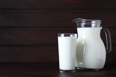 Photo of Jug and glass with fresh milk on wooden table. Space for text