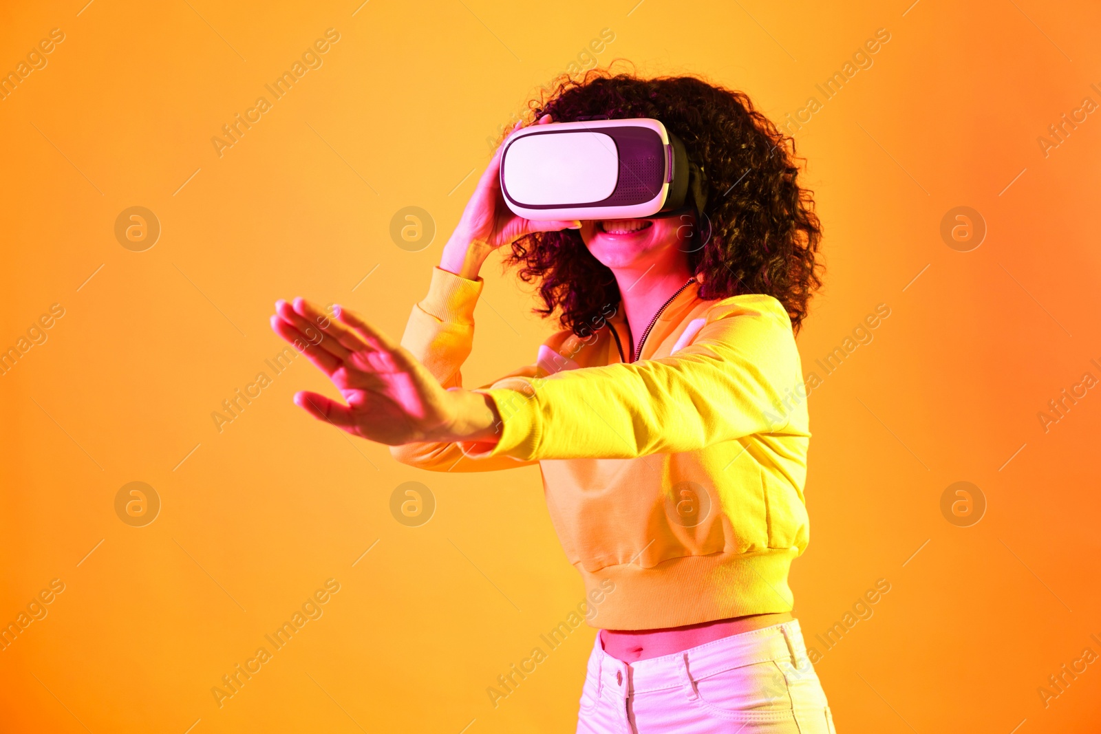 Photo of Beautiful young woman with virtual reality headset on color background in neon lights