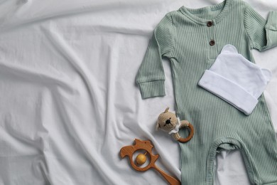 Photo of Flat lay composition with cute baby clothes and accessories on white bedsheet, space for text