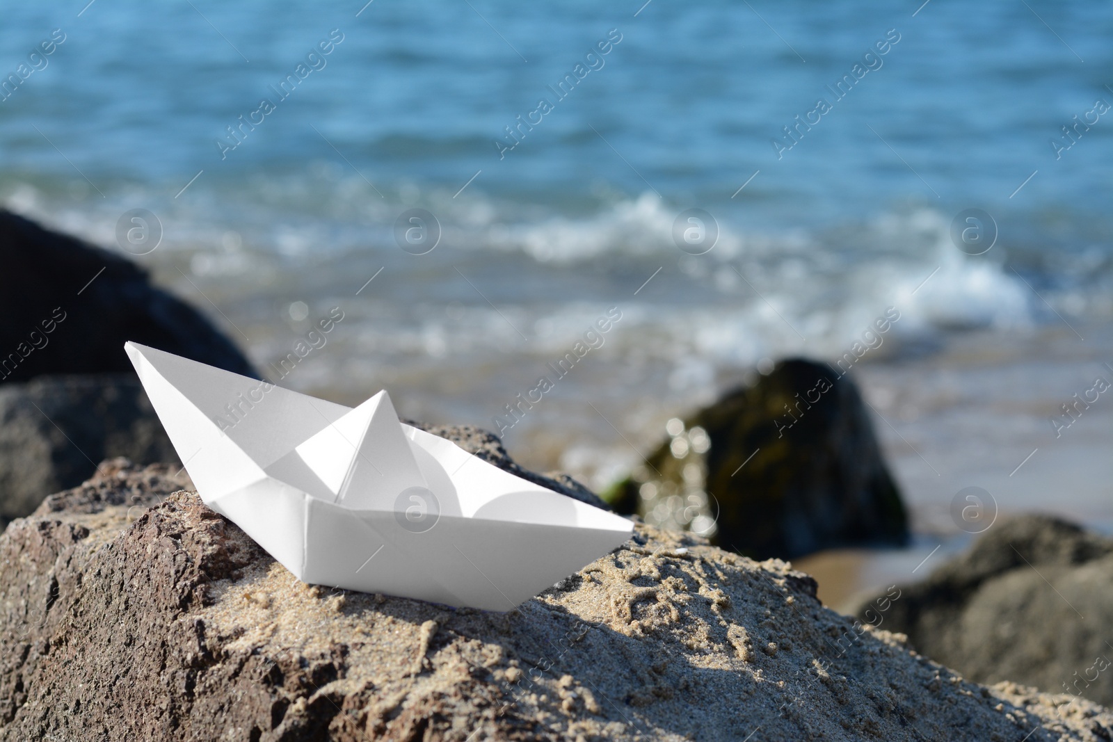 Photo of White paper boat on rock near sea, space for text