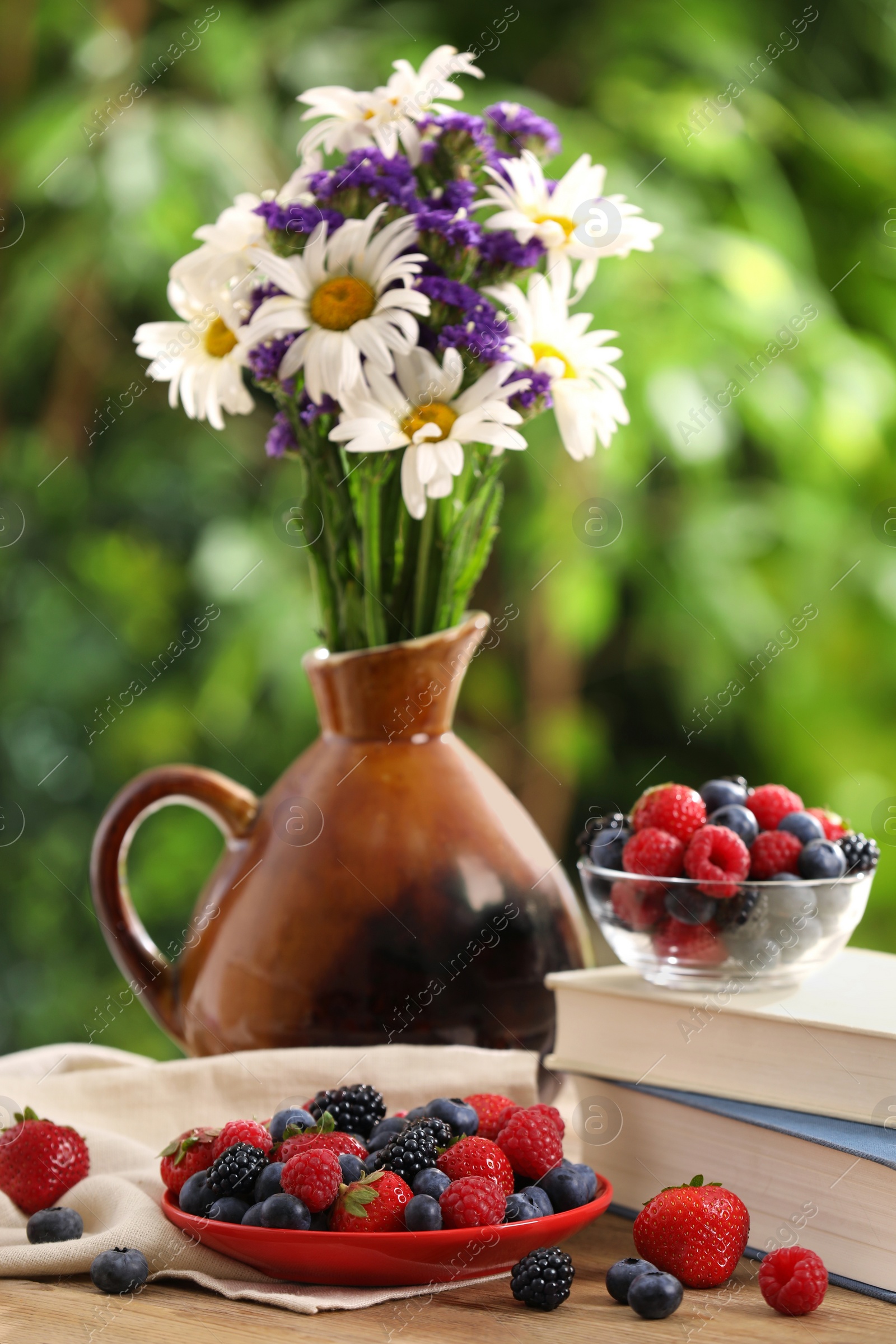 Photo of Different fresh ripe berries, beautiful flowers and books on wooden table outdoors