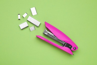 Photo of New bright stapler with staples on green background, fat lay. School stationery