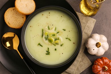 Photo of Bowl of tasty leek soup, spoon and bread on grey table, flat lay