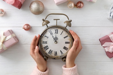 Woman with alarm clock near Christmas decor on white wooden background, top view. New Year countdown