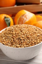 Bowl with dried orange seasoning zest and fruits on white wooden table, closeup