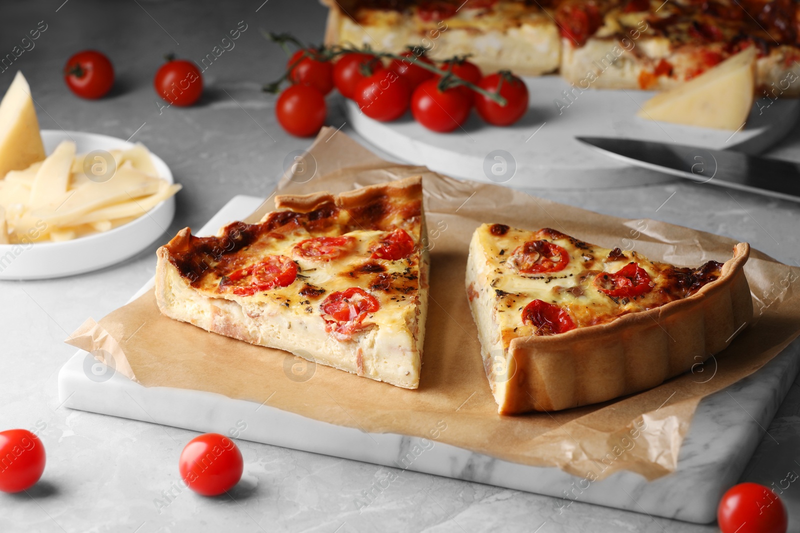 Photo of Pieces of delicious homemade quiche with prosciutto and tomatoes on light grey marble table