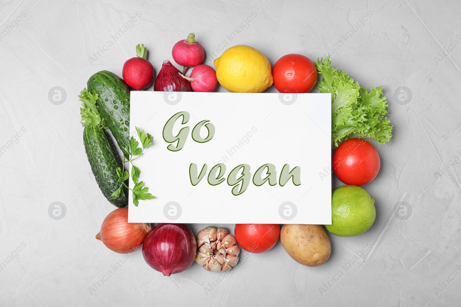 Image of Paper card with phrase Go Vegan and fresh vegetables on light grey background, flat lay