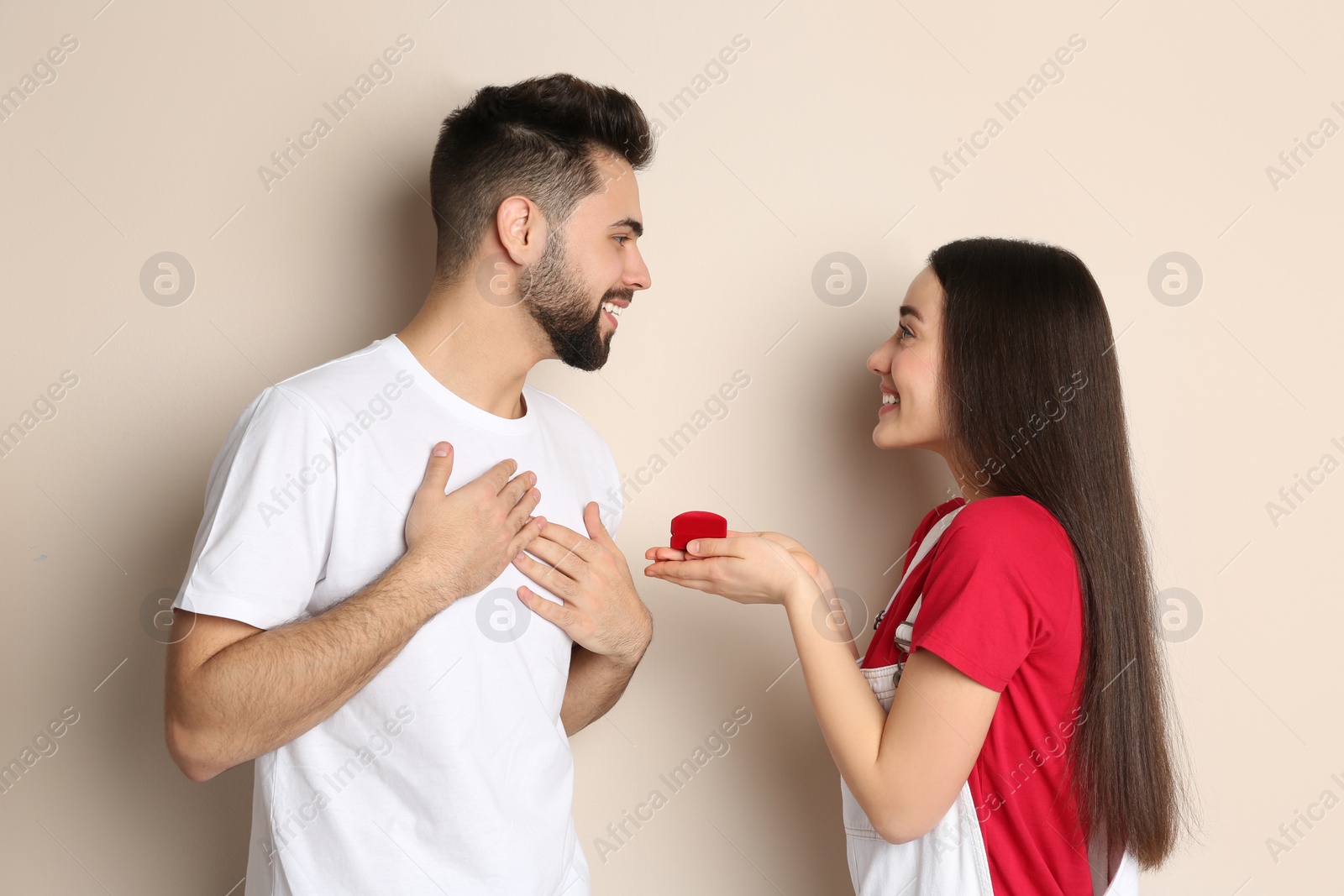 Photo of Young woman with engagement ring making marriage proposal to her boyfriend on beige background