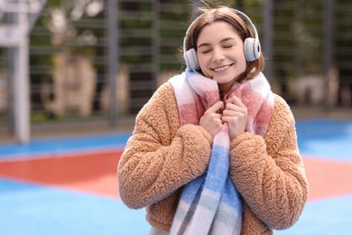 Photo of Beautiful woman in warm scarf listening to music outdoors, space for text