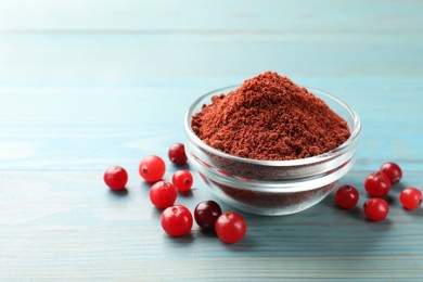 Photo of Cranberry powder in bowl and fresh berries on light blue wooden table, closeup. Space for text