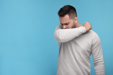 Sick man coughing on light blue background, space for text