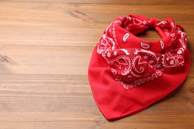 Photo of Tied red bandana with paisley pattern on wooden table, space for text