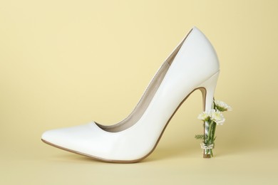 Photo of Stylish women's high heeled shoe with beautiful flowers on pale yellow background
