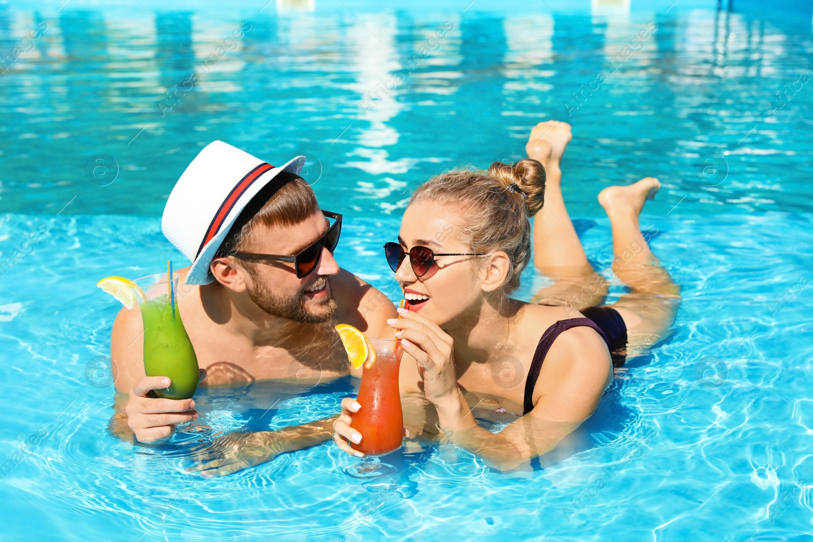 Photo of Young couple with refreshing cocktails in swimming pool at resort