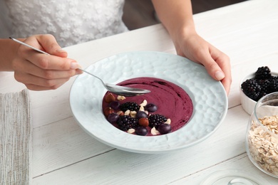 Photo of Woman eating tasty acai smoothie at table, closeup