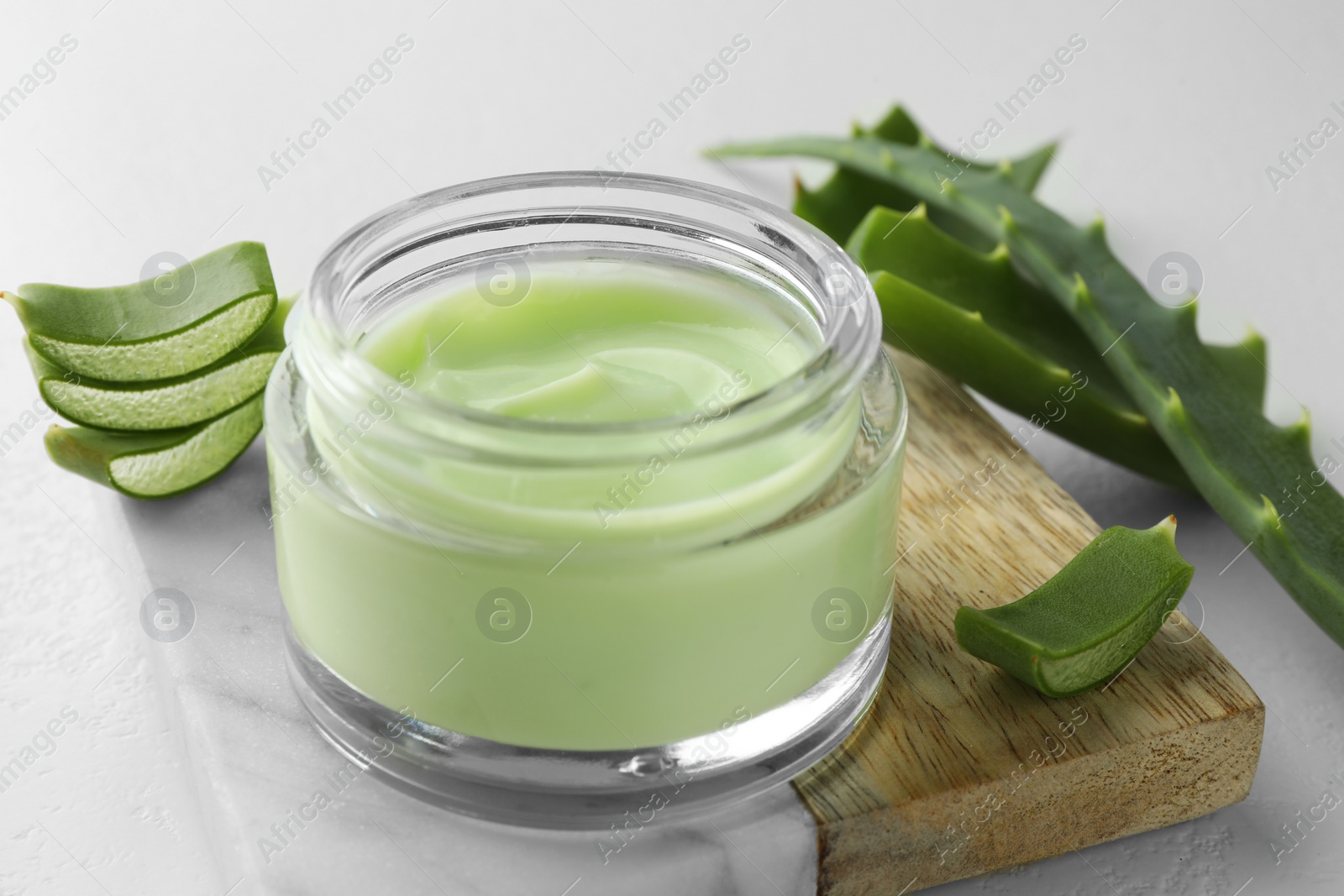 Photo of Jar with cream and cut aloe leaves on white table, closeup