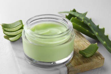 Photo of Jar with cream and cut aloe leaves on white table, closeup