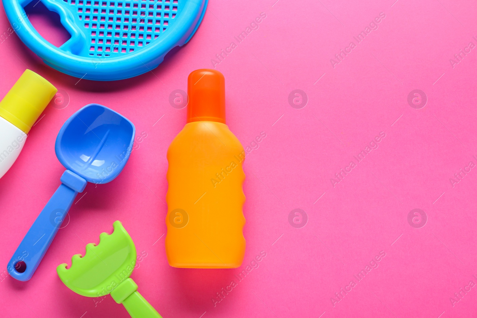 Photo of Bottle of suntan cream and children's beach toys on pink background, flat lay. Space for text