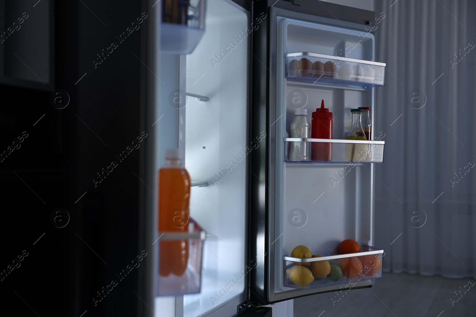 Photo of Open refrigerator full of different products in kitchen