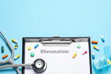 Clipboard with word Rheumatism, stethoscope and pills on light blue background, flat lay. Space for text