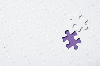 Photo of Blank white puzzle with separated piece on purple background, top view. Space for text