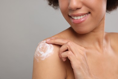 Young woman applying body cream onto shoulder on grey background, closeup. Space for text