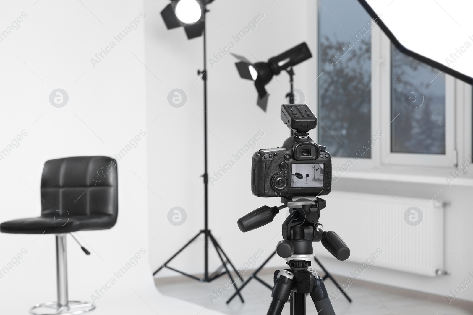 Photo of Camera on tripod, bar stool and professional lighting equipment in modern photo studio, space for text