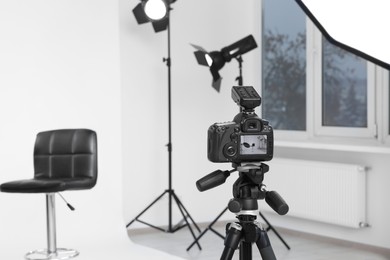 Photo of Camera on tripod, bar stool and professional lighting equipment in modern photo studio, space for text