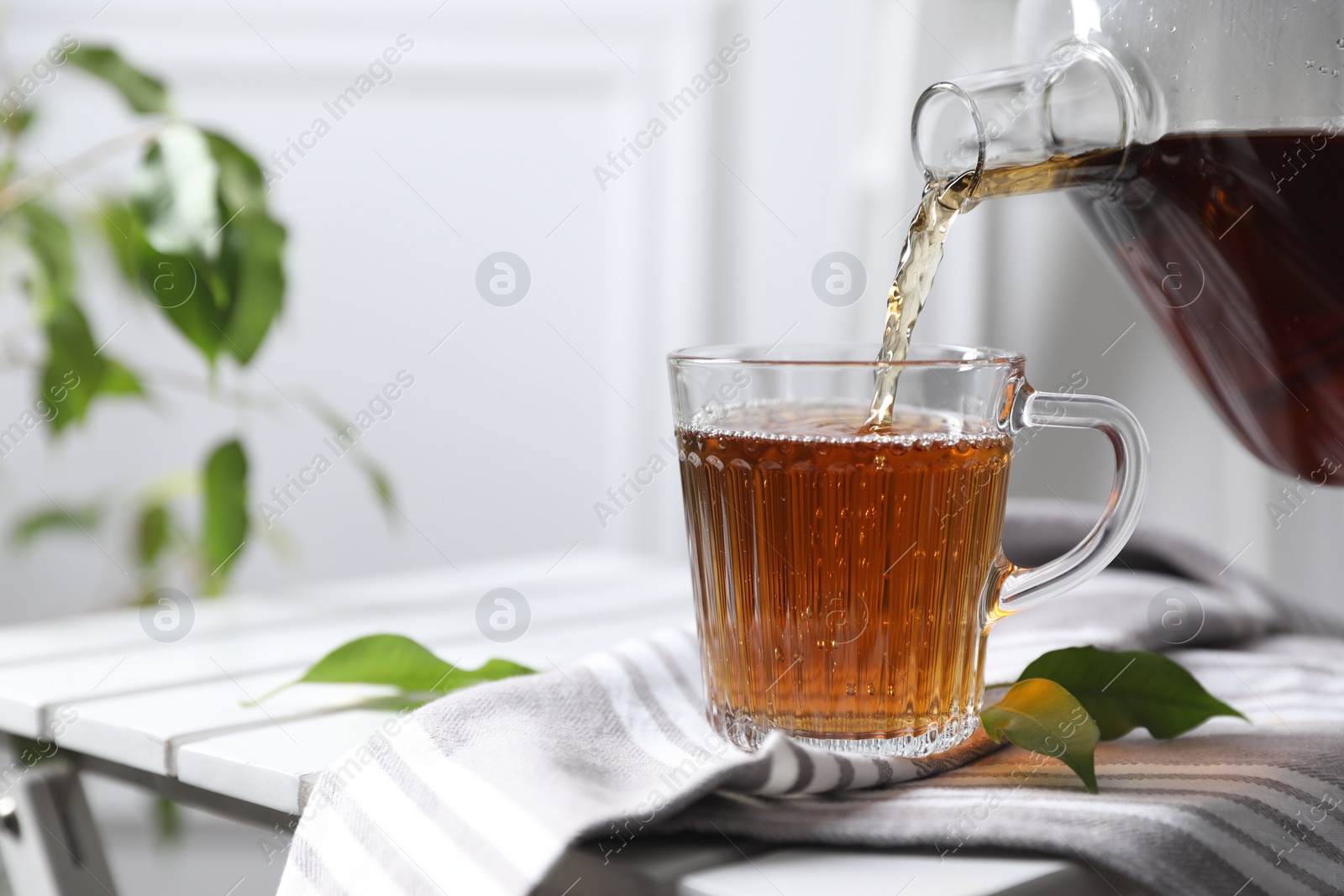 Photo of Pouring hot tea into cup on table, closeup