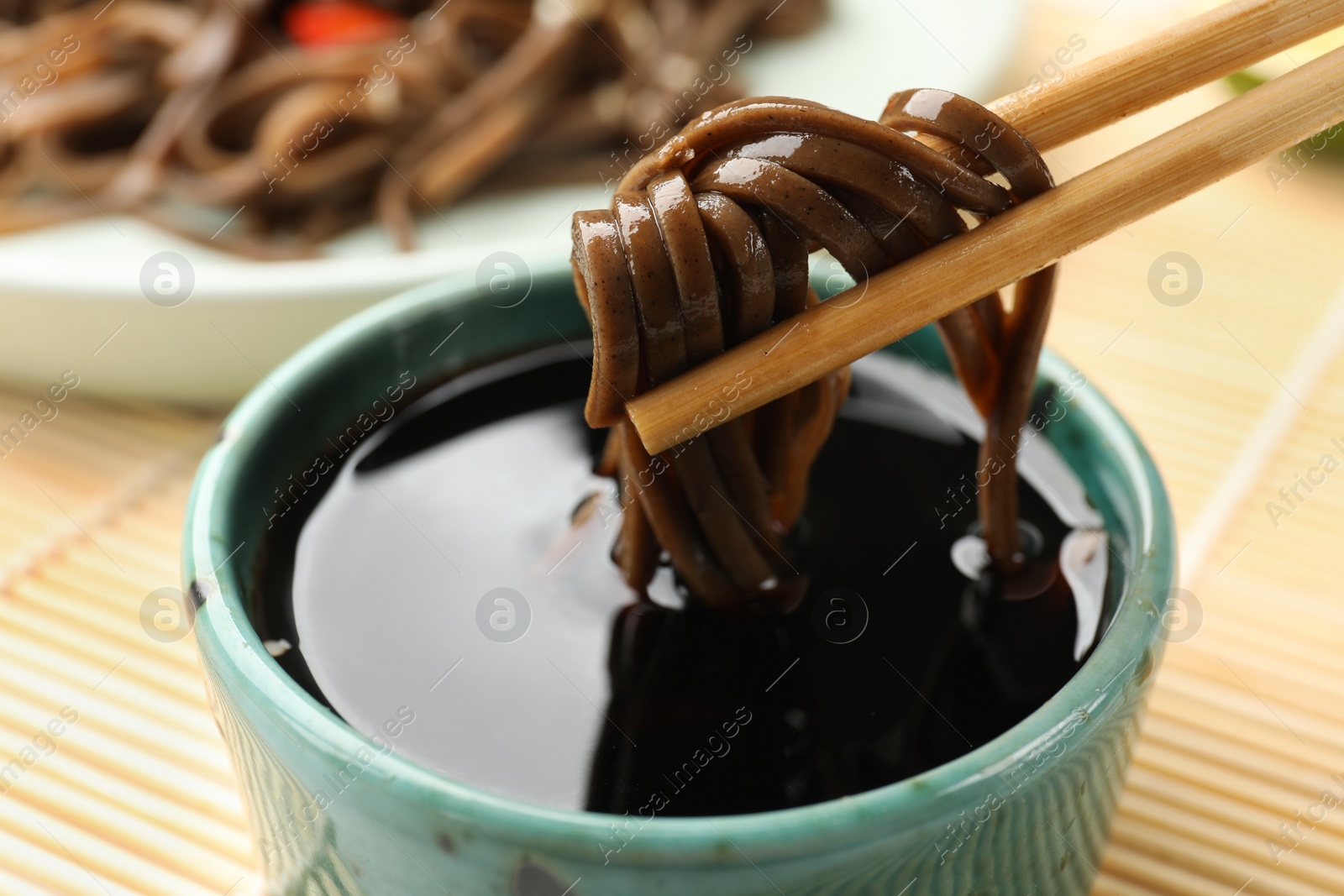 Photo of Eating delicious buckwheat noodles (soba) with chopsticks at table, closeup