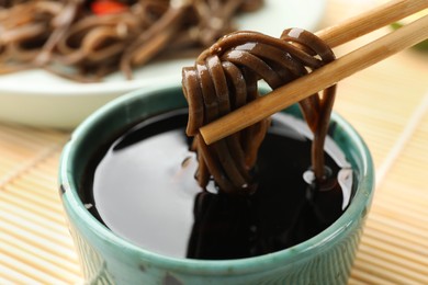 Photo of Eating delicious buckwheat noodles (soba) with chopsticks at table, closeup